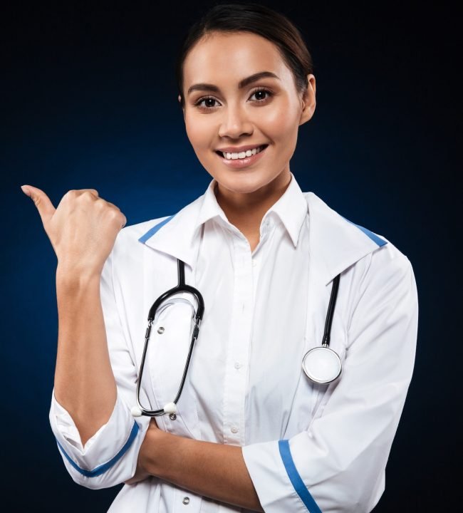 Young happy lady with stethoscope looking camera and pointing at copy space isolated over black